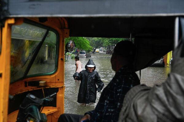 صورة تظهرامرأة في لباس صيفي تمشي في شارع غمره المياه، ويظهر أيضا رجل في رداء أسود مطري. - سبوتنيك عربي
