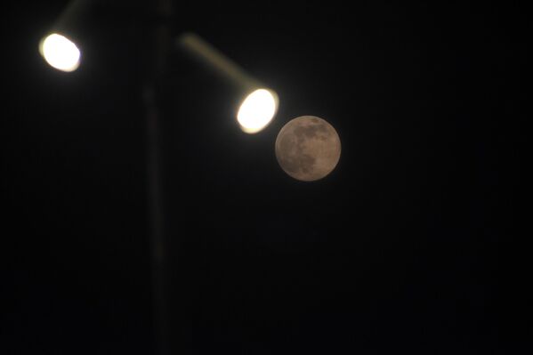 القمر العملاق الأخير، المعروف أيضا باسم &quot;القمر البارد&quot;، يرتفع خلف أضواء الشوارع في سريناغار، كشمير، الهند - سبوتنيك عربي