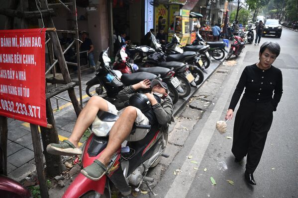 إحدى شوارع هانوي في فيتنام، وتظهر الصورة أحد الأشخاص مستلقيا على دراجته النارية، وِشخصا آخر يرتدي لباسًا أسودًا ويحمل بيده كيسا صغيرا. - سبوتنيك عربي