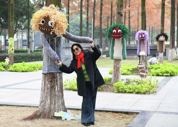 امرأة تظهر بالقرب من إحدى الأشجار التي تم تزيينها بـ &quot;لباس ملون&quot; في فصل الشتاء وتظهر المرأة وهي تمسك يدي الشجرة التي تم تزيينها. - سبوتنيك عربي