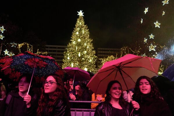 العاصمة اليونانية، أثينا، تضيئ شجرة عيد الميلاد بينما يستمع الناس إلى حفل موسيقي أثناء هطول الأمطار. - سبوتنيك عربي