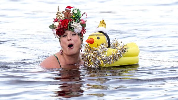 Участница группы любителей плавания в открытой воде Loch Insh Dippers принимает участие в рождественском заплыве в озере Лох-Инш в национальном парке Кэрнгормс, Шотландия - سبوتنيك عربي