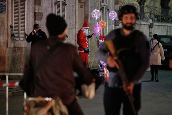 رجل يرتدي زي "بابا نويل" في سوريا يبيع زينة عيد الميلاد، بينما يقف الأمن السوري على مقربة منه في حي القصاع في دمشق - سبوتنيك عربي