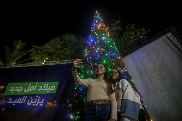 أشخاص يقفون أمام شجرة عيد الميلاد في كنيسة "العائلة المقدسة" في غزة - سبوتنيك عربي