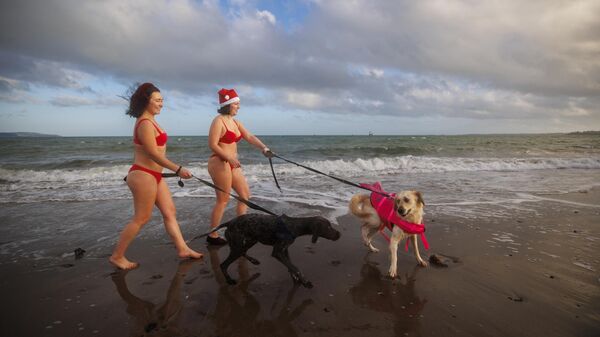 Девушки идут по пляжу Хелен-Бей после участия в ежегодном рождественском заплыве в поддержку местных благотворительных организаций, США - سبوتنيك عربي