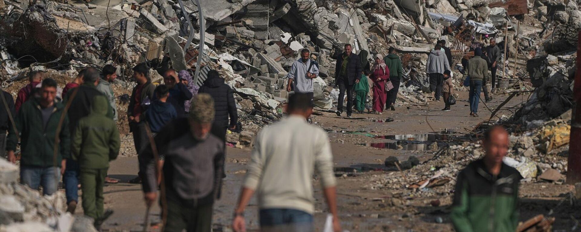 فلسطينيون يسيرون في شارع محاط بمبان دمرت خلال عمليات جوية وبرية إسرائيلية في مدينة غزة، 17 ديسمبر/ كانون الأول 2025 - سبوتنيك عربي, 1920, 28.12.2025