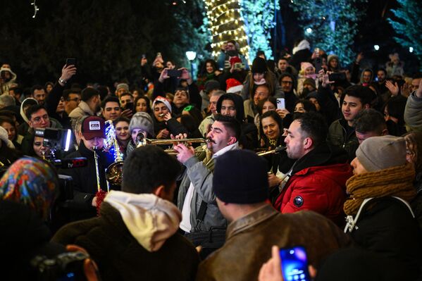 صورة تظهر أشخاصا يلتقطون صورًا تذكارية مع آخرين يرتدون أزياء بابا نويل وسط زينة رأس السنة المضاءة في حديقة "كوغولو"، بمنطقة "جانكايا"، في أنقرة، تركيا. - سبوتنيك عربي