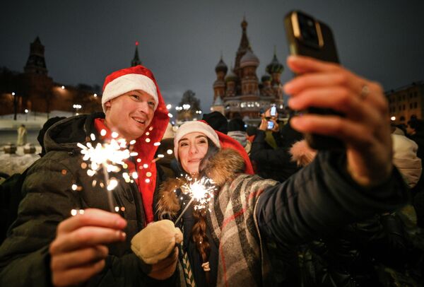 الاحتفالات في الساحة الحمراء، ويظهر في الصورة شاب وفتاتة وهما يستعدان لالتقاط صورة سيلفي ويمسكان بأيديهم شمع ذو أضواء. - سبوتنيك عربي