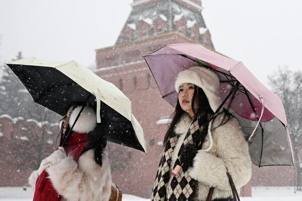 سائحتان تحملان مظلة خلال تساقط الثلوج في الساحة الحمراء وسط موسكو - سبوتنيك عربي