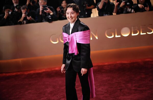 بيلا رامزي على السجادة الحمراء،  ترتدي بدلة رسمية سوداء وتلفّ ذراعيها بقماش زهري من الساتان. - سبوتنيك عربي