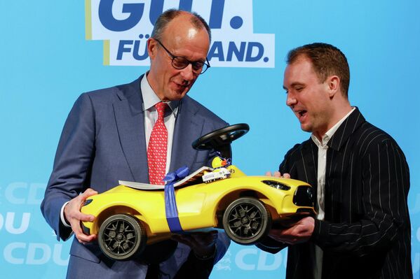 تسلّم المستشار الألماني فريدريش ميرز سيارة لعبة لأبنائه من موظف في مجموعة بفينينغ، خلال حملة انتخابية لمانويل هاغل، المرشح الأبرز عن حزب الاتحاد الديمقراطي المسيحي في ولاية بادن فورتمبيرغ، في مدينة هيدسهايم الألمانية، بتاريخ 16 يناير/كانون الثاني 2026. - سبوتنيك عربي