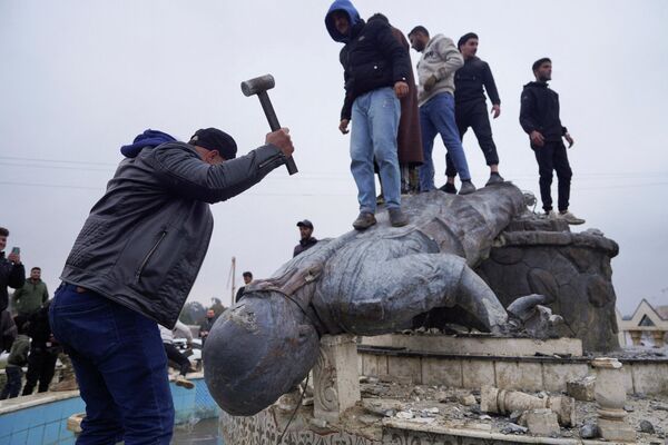 مجموعة من المدنيين يحطمون تمثالاً لمقاتل من قوات سوريا الديمقراطية "قسد"  في مدينة الطبقة شمالي سوريا، بعد سيطرة الجيش السوري عليها. - سبوتنيك عربي