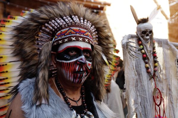 مشارك في كرنفال "الزامبو" يطلو وجهه بالأحمر والأسود والأبيض ويضع على رأسه ريشا عل ىشكل دائرة، وبجواره تظهر دمية على شكل الشبخ. - سبوتنيك عربي