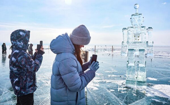 مشاركون في مهرجان فنون الجليد الشتوي الـ12، مباشرة على بحيرة "بايكال"، في قرية ليستفيانكا، بالقرب من مجسم روبوت جليدي - سبوتنيك عربي