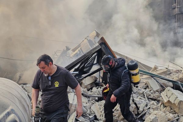 رجال إطفاء يسيرون بين الأنقاض، بينما يتصاعد الدخان من أحد المباني الذي تم استهدافه بغارة جوية إسرائيلية في الضاحية الجنوبية. - سبوتنيك عربي