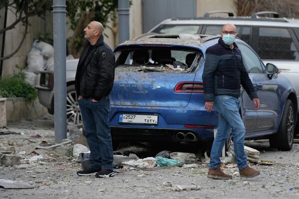 أشخاص يتفقدون موقع فندق متضرر تعرض لغارة جوية إسرائيلية في الحازمية، شرقي بيروت، وتظهر في الشارع سيارة متضررة بشكل كبير نتيجة الشظايا. - سبوتنيك عربي