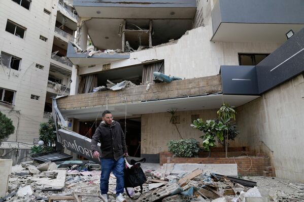 رجل يحمل أمتعته أثناء مغادرته فندقا متضررا نتيجة استهدافه بغارة جوية إسرائيلية في الحازمية. - سبوتنيك عربي