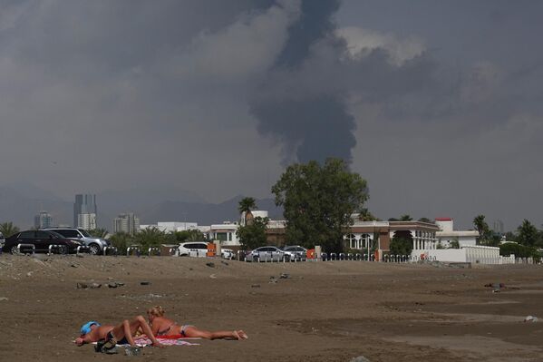 يستلقي الناس على الشاطئ بينما يتصاعد الدخان فوق منطقة الصناعات النفطية في الفجيرة في الإمارات العربية المتحدة، بعد اندلاع حريق ناجم عن سقوط حطام طائرة مسيّرة اعترضتها الدفاعات الجوية، وذلك على خلفية الحرب الجارية بين الولايات المتحدة وإسرائيل وإيران. - سبوتنيك عربي