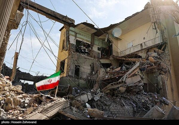 دمار كبير في الأبنية السكنية نتيجة الغارات الأمريكية - الإسرائيلية، ويظهر العلم الإيراني مثبتًا فوق الأنقاض، في رمزية لصمود أبناء المنطقة - سبوتنيك عربي