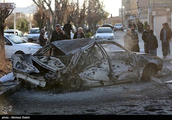 أشخاص يقفون إلى جانب سيارة متضررة بشكل كامل نتيجة الغارات الأمريكية - الإسرائيلية، التي استهدفت العاصمة طهران  - سبوتنيك عربي