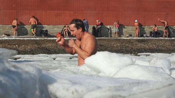 Мужчина плавает в ледяной воде, в то время как другие загорают у стен Петропавловской крепости в Санкт-Петербурге, Россия - سبوتنيك عربي