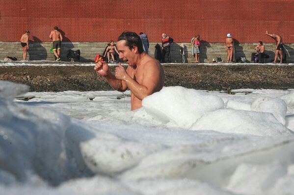 رجل يسبح في المياه الجليدية، بينما يستمتع آخرون بحمامات الشمس عند جدار قلعة القديسين بطرس وبولس في سانت بطرسبرغ. - سبوتنيك عربي
