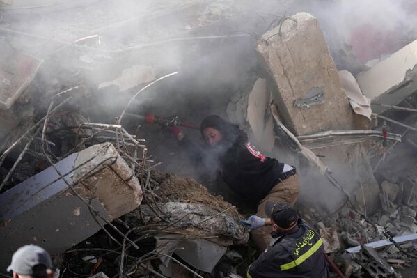 رجل إطفاء يرش الماء للحد من الغبار، بينما يبحث عمال الإنقاذ عن ضحايا في مبنى مدمر تعرض لغارة جوية إسرائيلية في بلدة غازية، جنوبي لبنان. - سبوتنيك عربي