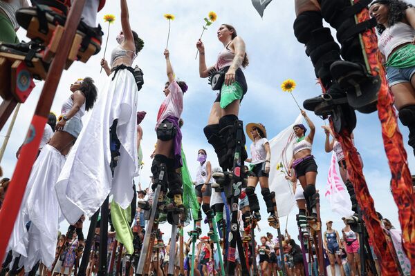نساء على ركائز خشبية، من مجموعة "غيغانتس نا لوتا"، يرفعن زهور عباد الشمس البلاستيكية في الهواء خلال مسيرة بمناسبة اليوم العالمي للمرأة في ريو دي جانيرو، البرازيل. - سبوتنيك عربي
