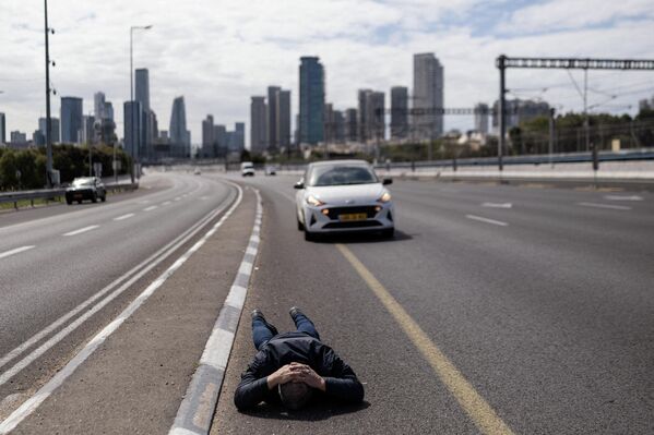 رجل يتمدد على طريق رئيسية في إسرائيل للاحتماء أثناء إطلاق صفارات الإنذار عقب وابل من الصواريخ الإيرانية. - سبوتنيك عربي