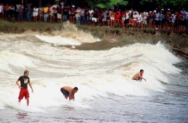  تُظهر هذه الصورة، من عام 2001، سكان قرية في جزيرة تويو بالقرب من ساو دومينغوس دو كابيم، شمال البرازيل، وهم يشاهدون راكبي الأمواج  يتحدّون موجة المد والجزر العاتية "بوروروكا" في 12 مارس. تحدث ظاهرة بوروروكا سنويًا من فبراير إلى مارس، عندما يرتفع مدّ المحيط عاليًا في مواجهة تيار نهر الأمازون، مُشكّلًا أمواجًا يصل ارتفاعها إلى 3 أمتار، تنتقل لمئات الأميال عكس التيار لمدة تصل إلى 45 دقيقة - سبوتنيك عربي