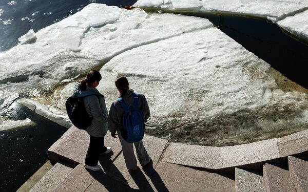 شابتان تقفان على درج حجري يطل على ضفاف نهر نيفا، في مشهد يعكس تفاعل السكان مع حلول فصل الربيع في المدينة. - سبوتنيك عربي