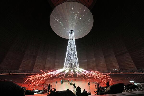 ينظر الناس إلى العمل الفني الضوئي والصوتي الشجرة الذي يبلغ ارتفاعه 35 متراً خلال افتتاح المعرض الجديد عوالم الغابات في المعلم الصناعي غازوميتر، الذي كان سابقا أكبر خزان غاز من النوع القرصي في أوروبا، في ألمانيا. - سبوتنيك عربي