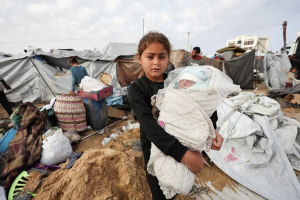 طفلة فلسطينية نازحة تحمل شقيقتها الرضيعة في موقع الغارة الإسرائيلية التي استهدفت مخيما للخيام يأوي نازحين فلسطينيين في مدينة غزة. - سبوتنيك عربي