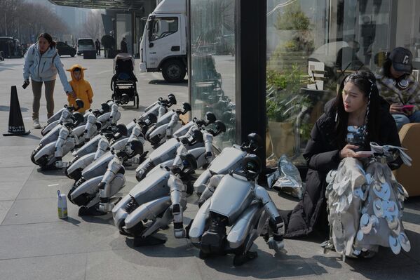 عارضة أزياء تستريح بالقرب من روبوتات تنتظر فعالية ترويجية في بكين. - سبوتنيك عربي