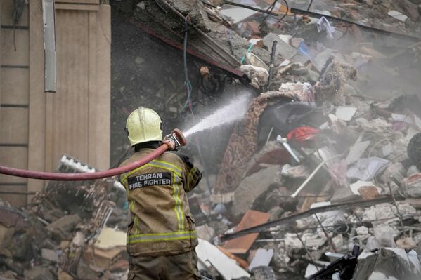 رجل الإطفاء يقوم برشّ الأنقاض المتفحمة بالماء بينما تقوم جرافة بإزالة الحطام من إحدى المباني السكنية التي تعرضت للقصف. - سبوتنيك عربي