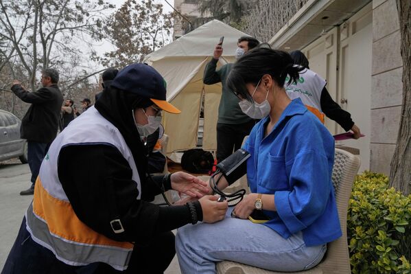 يقوم أحد المسعفين بقياس ضغط دم امرأة في أحد المواقع التي تعرضت للقصف الأمريكي الإسرائيلي في العاصمة طهران. - سبوتنيك عربي