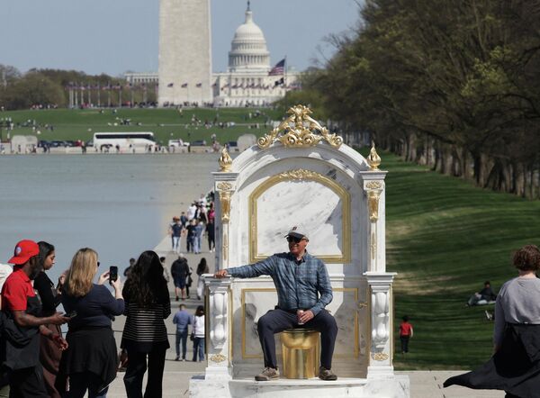 رجل يجلس على تمثال لمرحاض ذهبي ضخم، يحمل عنوان "عرش يليق بملك"، معروض بالقرب من نصب لنكولن التذكاري في ناشونال مول بواشنطن العاصمة، الولايات المتحدة الأمريكية، 30 مارس 2026 - سبوتنيك عربي