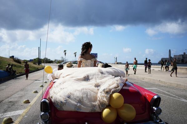 فتاة تستقل سيارة كلاسيكية في أحد الشوارع، خلال احتفالها بعيد ميلادها في هافانا، كوبا. - سبوتنيك عربي