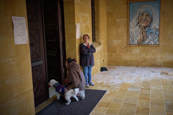 امرأة تركع بجانب كلبها عند مدخل كنيسة كاثوليكية خلال قداس أحد الشعانين في العاصمة اللبنانية، بيروت. - سبوتنيك عربي