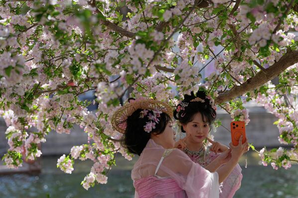 تلتقط نساء يرتدين أزياء تقليدية صور "سيلفي" على ضفاف نهر في حديقة عامة في بكين، وسط أجواء ربيعية ساحرة خلال موسم تفتح أزهار الكرز. - سبوتنيك عربي