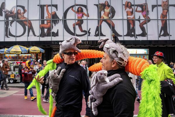 رجلان يحملان أرنبين على صدورهما بينما يضعان مجسمين ضخمين من الجزر على كتفيهما، وذلك خلال مشاركتهما في موكب قبعات عيد الفصح  في نيويورك. - سبوتنيك عربي