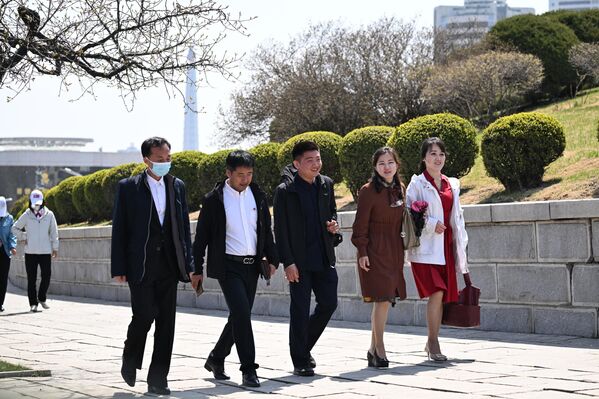 شباب وفتيات يسيرون في أحد شوارع العاصمة بيونغ يانغ، إلى جانب حديقة تتزين أشجارها بحلّتها الخضراء. - سبوتنيك عربي