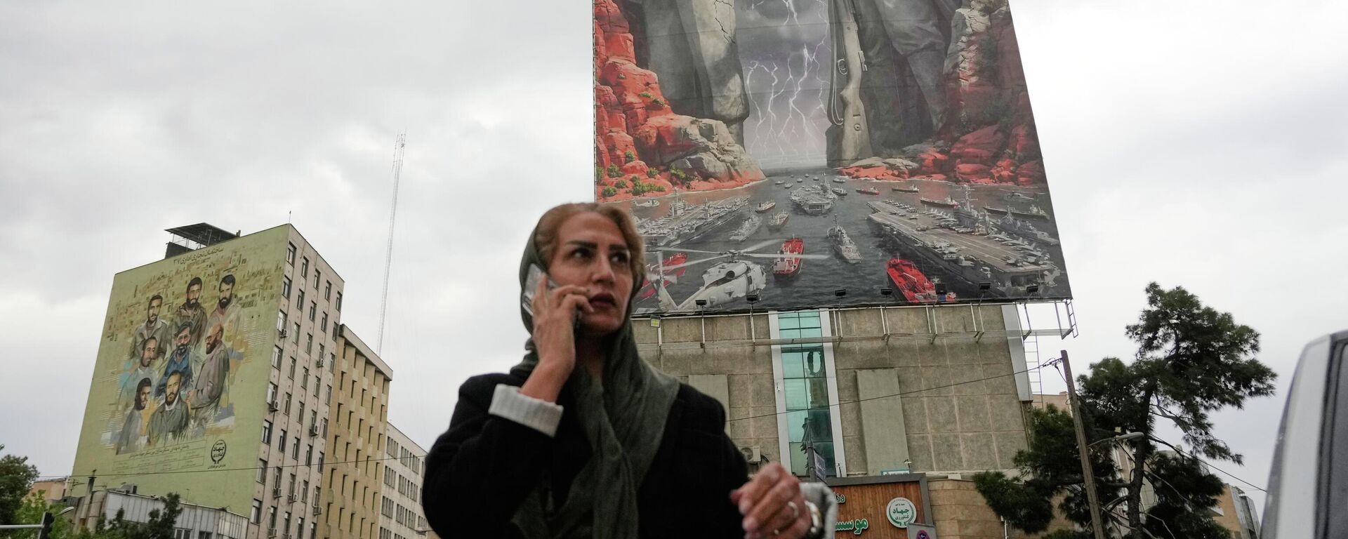 Женщина c мобильным телефоном на фоне плаката с изображением иранского военачальника Раиса-Али Дельвари и командующего ВМС КСИР Алирезы Тангсири в Тегеране, Иран - سبوتنيك عربي, 1920, 22.04.2026