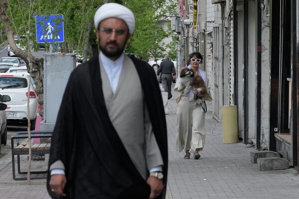 أحد رجال الدين الإيرانيين يسير في أحد شوارع العاصمة طهران، وتظهر خلفه سيدة تحمل كلبها. - سبوتنيك عربي