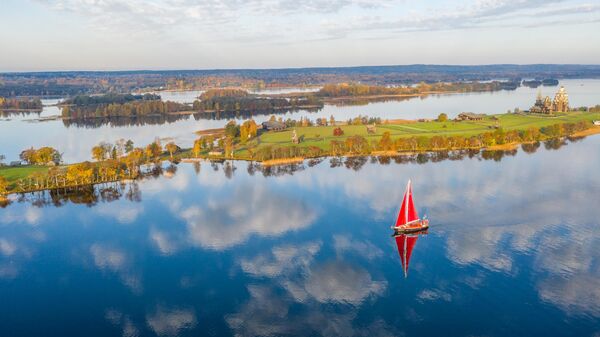 صورة تظهر يخت الرحلات "بيتر الأكبر" قبالة جزيرة كيزهي، وخلفه تبرز كنائس التجلي وشفاعة العذراء وبرج الجرس، ضمن المجمع المعماري لمتحف كيزهي التاريخي في كاريليا. - سبوتنيك عربي