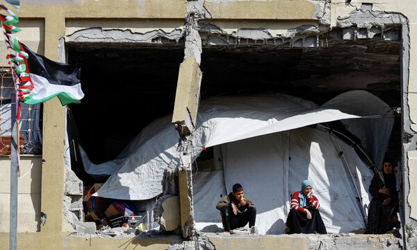 فلسطينيون يشاهدون من منازلهم المدمرة حفل زفاف جماعي لخمسين زوجًا نظمته مؤسسة الإغاثة الإنسانية (IHH) في مدينة غزة - سبوتنيك عربي