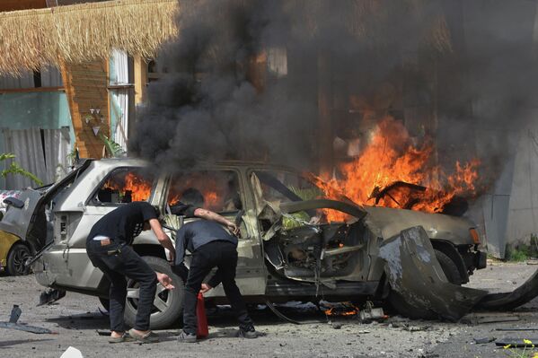 صورة توثق احتراق سيارة في لبنان، جراء غارة جوية إسرائيلية، حيث يظهر شخص داخل السيارة المحترقة، بينما يحاول رجال إخماد الحريق - سبوتنيك عربي