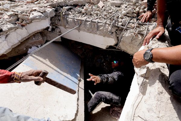 شخص يقوم بإعطاء مطرقة لرجل أثناء بحثهما عن ضحايا تحت أنقاض مبنى بعد الزلزال في لا غوايرا، فنزويلا - سبوتنيك عربي