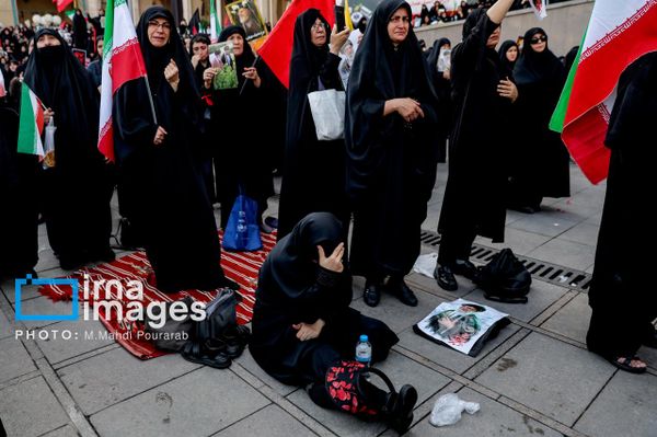 تُظهر اللقطة امرأة تبكي وهي تفترش الطريق، فيما تحمل نساء أخريات الأعلام الإيرانية خلال مراسم التشييع. - سبوتنيك عربي