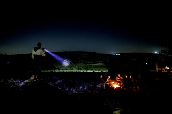 صورة تظهر رجل يستخدم مصباحًا يدويًا بينما يجلس متطوعون فلسطينيون آخرون حول نار موقدة لحماية بلدتهم من هجمات المستوطنين الإسرائيليين، في سنجيل، قرب رام الله، بالضفة الغربية المحتلة. - سبوتنيك عربي